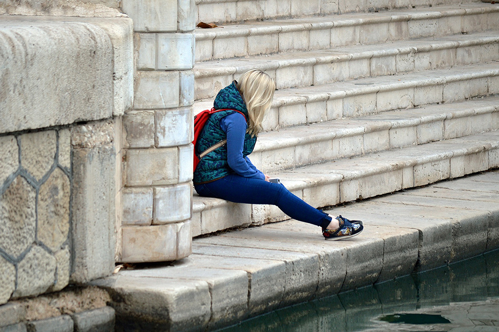 Eine Frau sitzt allein auf einer Treppe am Wasser