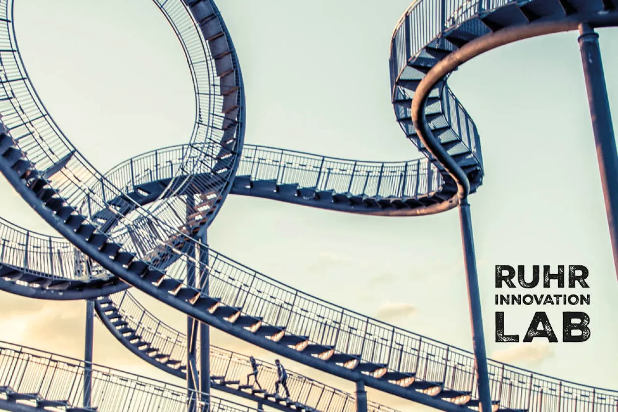 Das Kunstwerk Tiger and Turtle im Sonnenaufgang, darauf ein Logo des Ruhr Innovation Lab