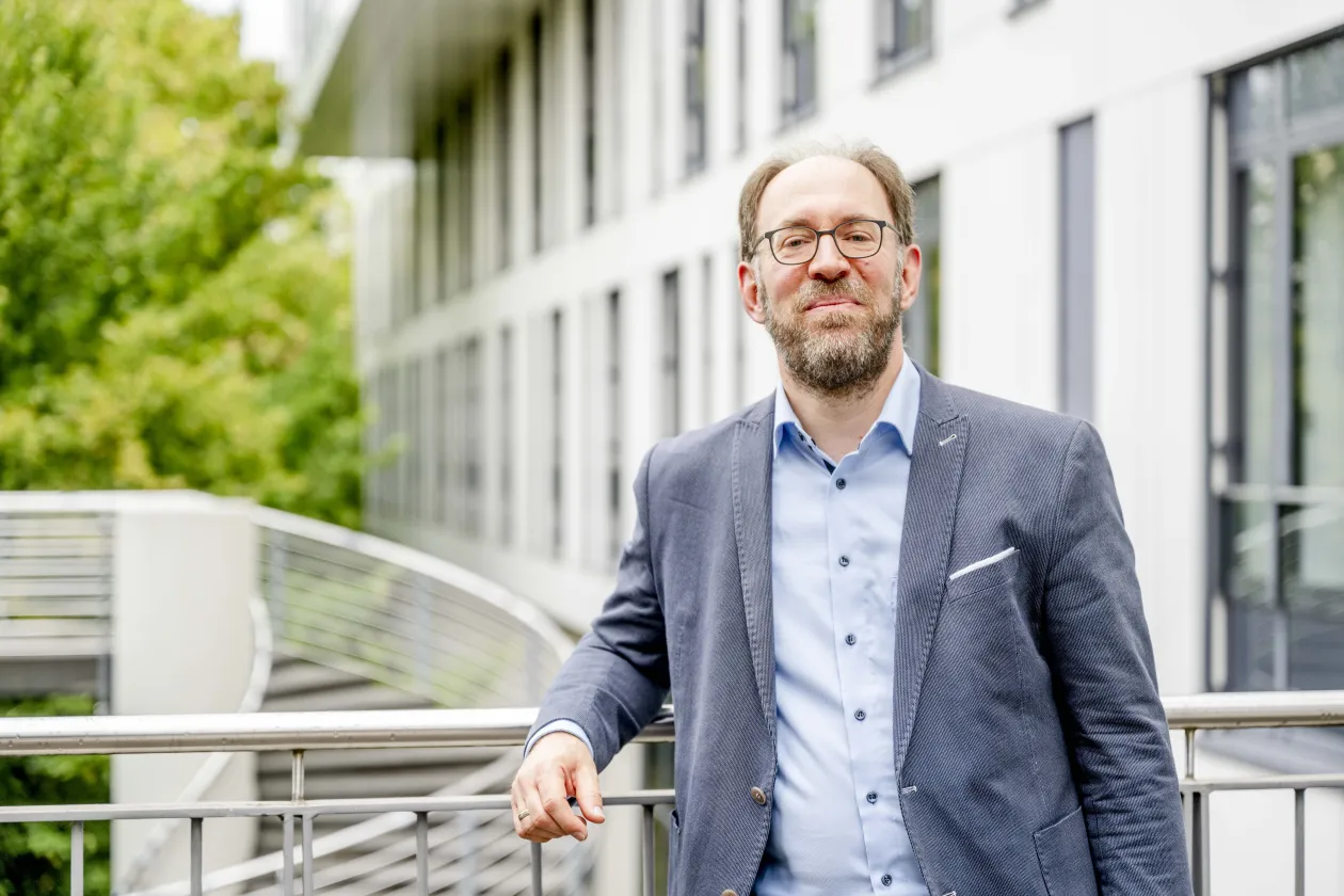 Ein Mann mit Brille im grauen Jackett lehnt an einer Brüstung