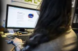 Frau sitzt vor einem Monitor, der die Webseite des DZPG zeigt