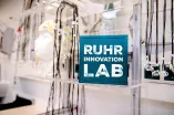 Ein Labor mit EEG-Kappe und Elektroden, darin ein türkisfarbener Würfel mit dem Schriftzug "Ruhr Innovation Lab"