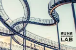Das Kunstwerk Tiger and Turtle im Sonnenaufgang, darauf ein Logo des Ruhr Innovation Lab