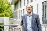 Ein Mann mit Brille im grauen Jackett lehnt an einer Brüstung
