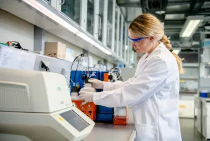 Eine Person in weißem Kittel schraubt im Labor eine Flasche zu.