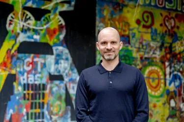 Mann im blauen Pullover vor einer bunt bemalten Wand