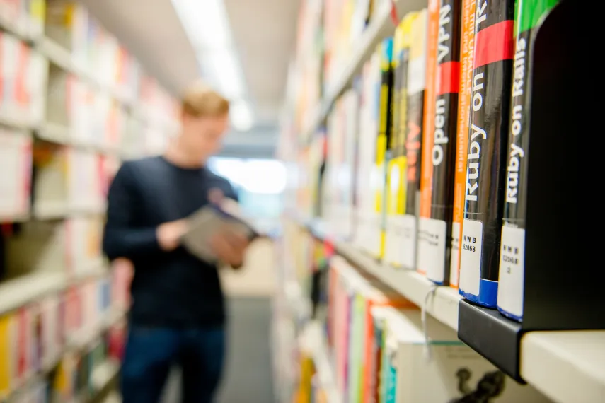 Mann in Bibliothek mit Büchern zur Informationstechnik