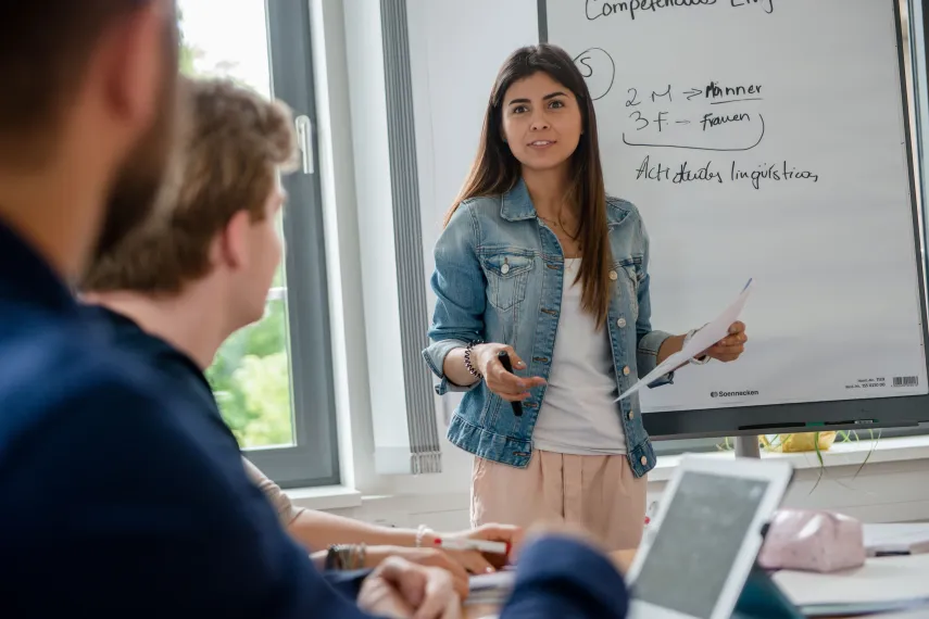 Eine junge Frau präsentiert etwas an einem Flipchart.