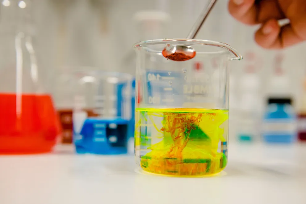 A red powder dissolves in a yellow liquid.