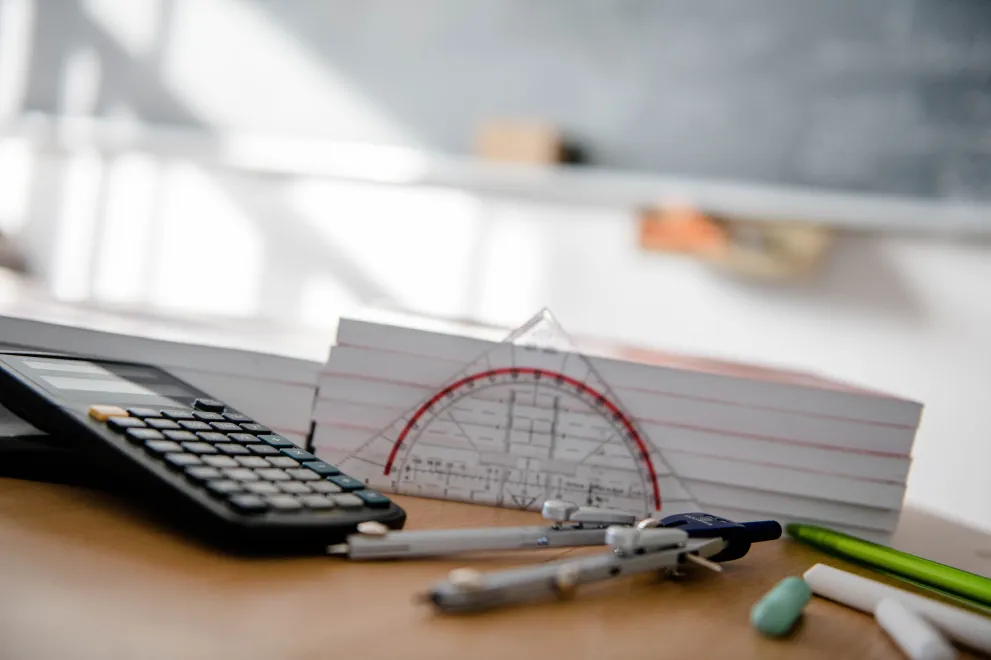 Taschenrechner und Geodreieck vor einer Tafel