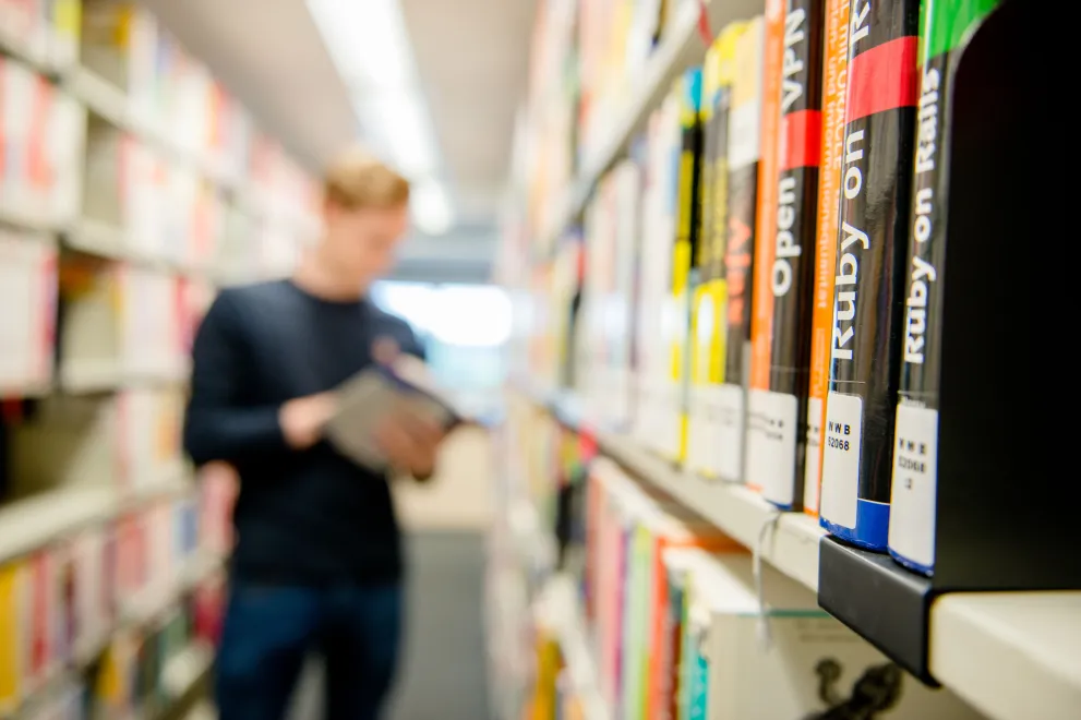 Mann in Bibliothek mit Büchern zur Informationstechnik