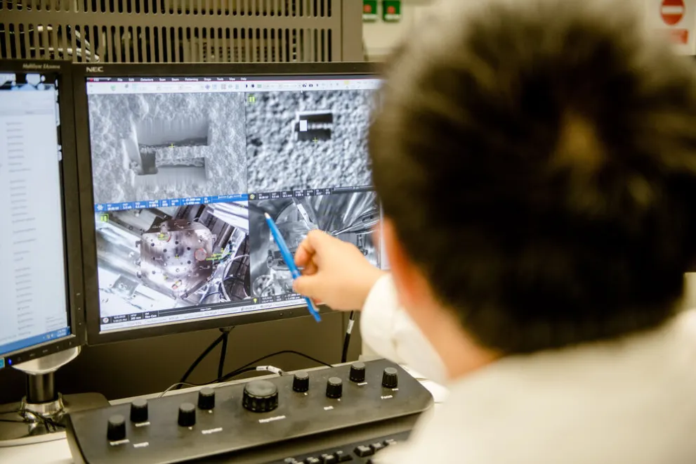 Jemand zeigt mit einem Kuli auf eine mikroskopische Aufnahme auf einem Monitor