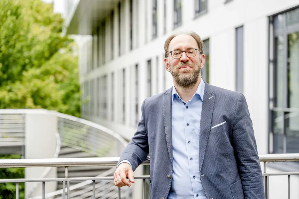 Ein Mann mit Brille im grauen Jackett lehnt an einer Brüstung