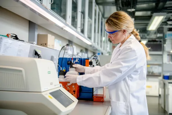 Eine Person in weißem Kittel schraubt im Labor eine Flasche zu.